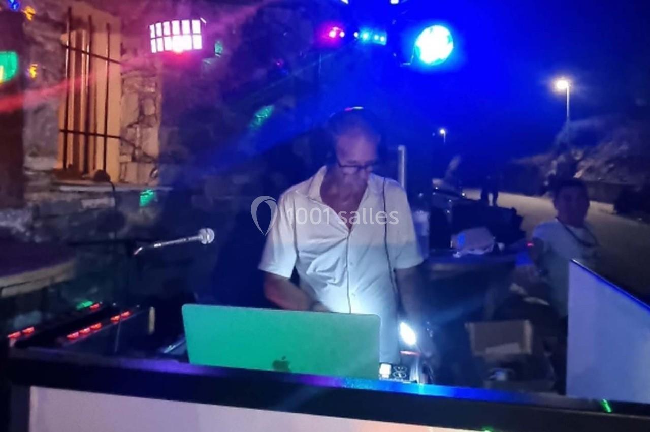 Un DJ mixe en extérieur de nuit, entouré de lumières colorées et d'équipements audio.