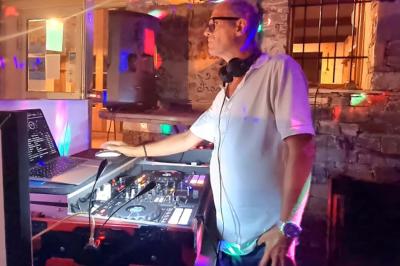 Un DJ mixe derrière une table éclairée par des lumières colorées dans une ambiance de soirée festive.
