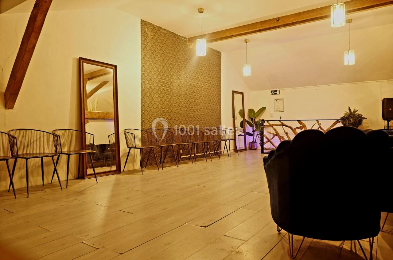 Salle lumineuse avec parquet clair, chaises alignées le long des murs, miroir et plantes en décoration.