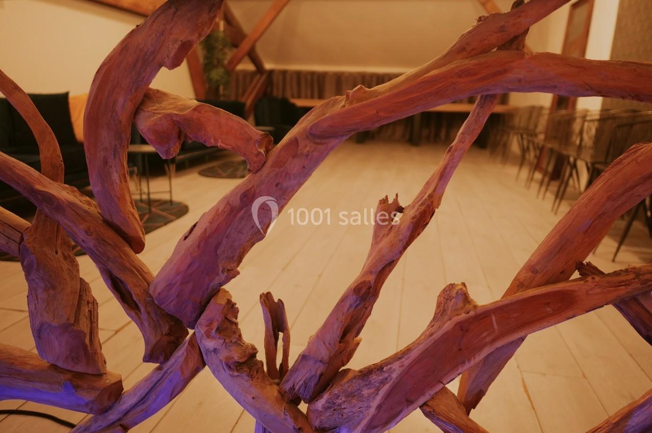 Structure en bois sculpté avec des branches entrelacées, devant une salle au sol clair et mobilier moderne.