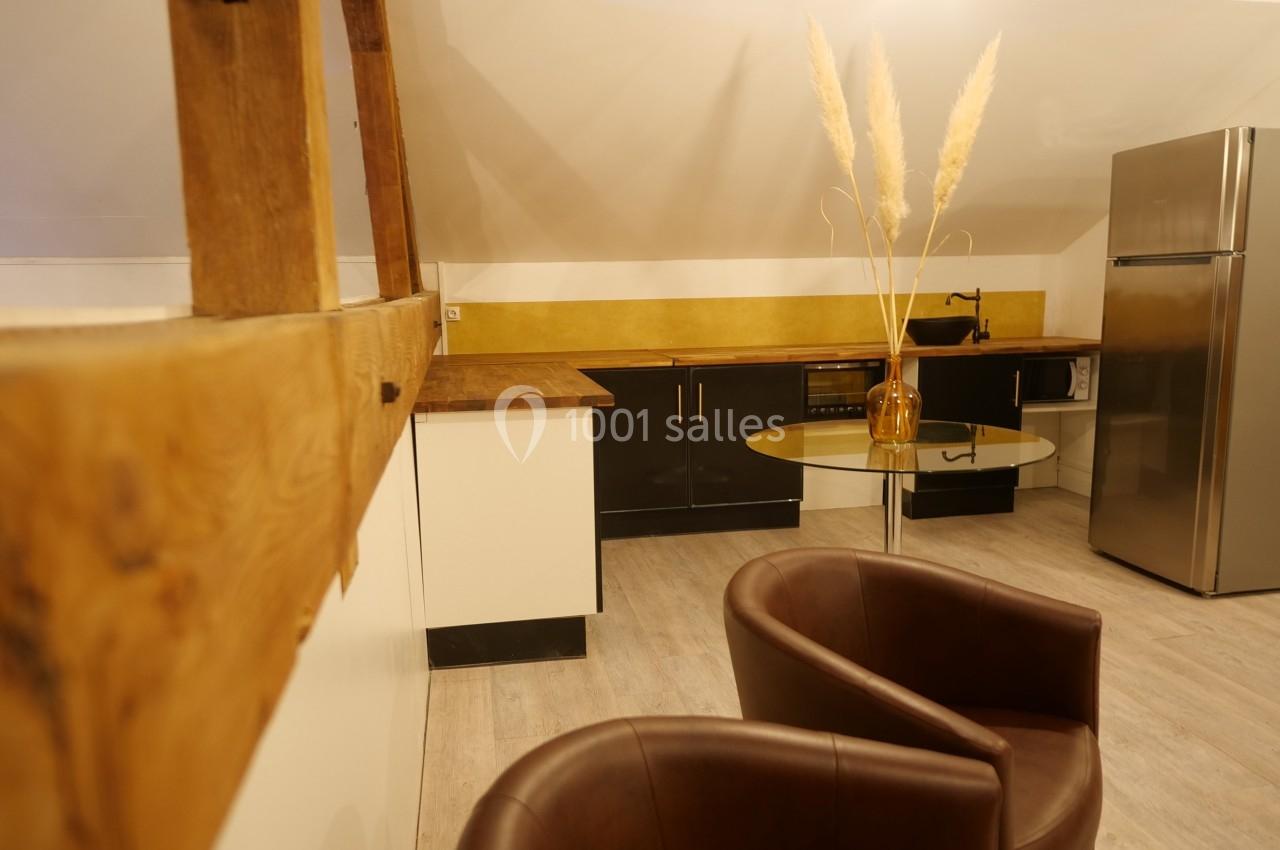 Cuisine mansardée avec comptoirs en bois, meubles noirs et blancs, table ronde, chaises en cuir et décoration minimaliste.