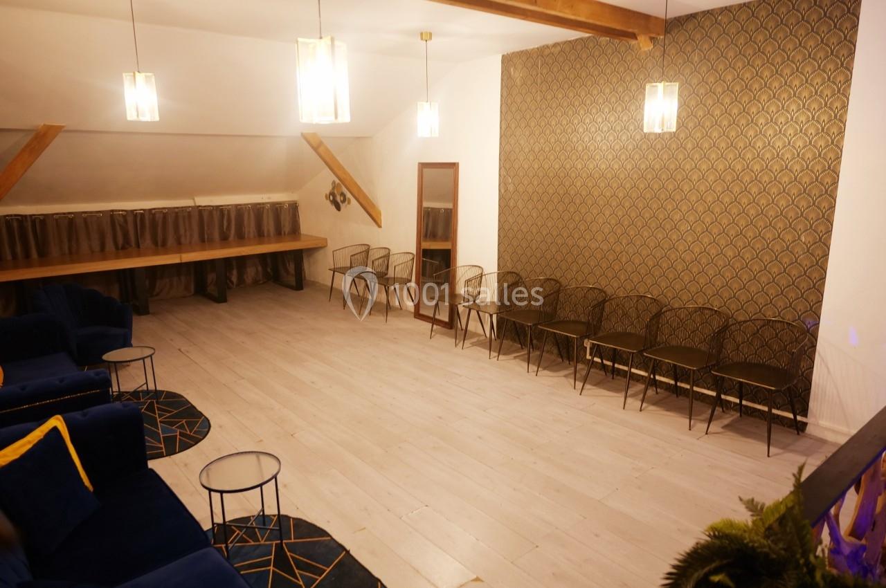 Salle lumineuse avec parquet clair, chaises alignées contre un mur décoré de motifs dorés et canapés bleus au premier plan.