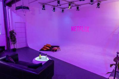 Miniature Rez-de-chaussée ESPACE PROJECTION Studio éclairé en violet avec un canapé, une table basse et des coussins au sol, logo Netflix projeté sur le mur.