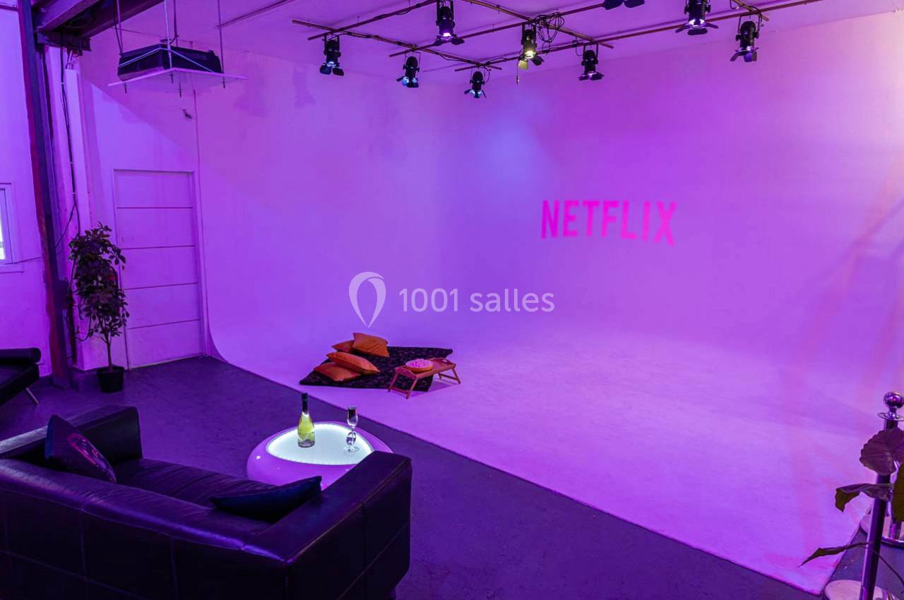 Studio éclairé en violet avec un canapé, une table basse et des coussins au sol, logo Netflix projeté sur le mur.
