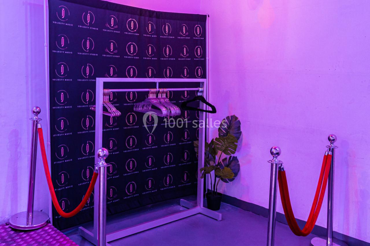 Portant avec cintres vides devant un fond noir à logo, entouré de cordons rouges et éclairé par une lumière violette.