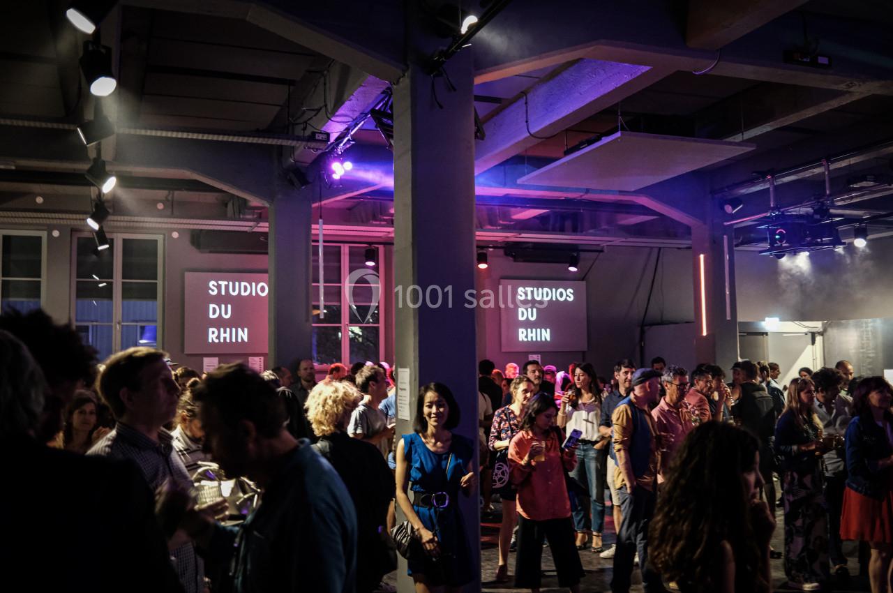 Salle animée avec des personnes debout discutant lors d'un événement, éclairée par des lumières colorées.