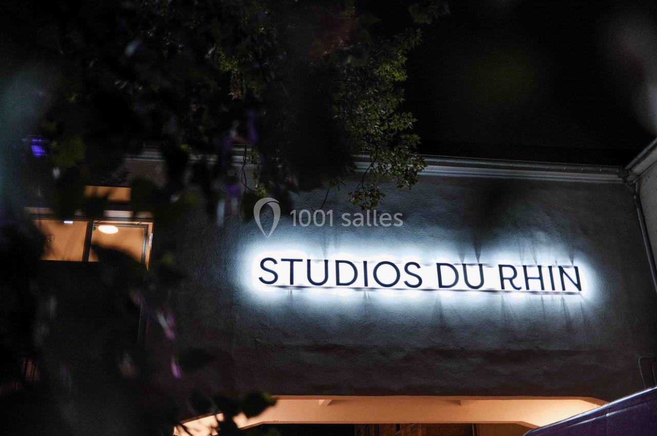 Enseigne lumineuse ’Studios du Rhin’ sur la façade d'un bâtiment, vue de nuit avec des branches en premier plan.