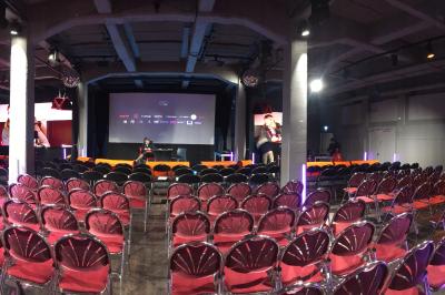 Un DJ mixe sur une scène éclairée par des lumières colorées, face à une foule dansante dans une salle sombre.