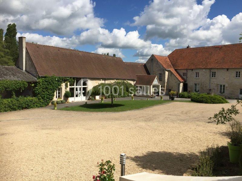 Cour d'une grande propriété en pierre avec toits en tuiles, entourée de verdure et sous un ciel partiellement nuageux.