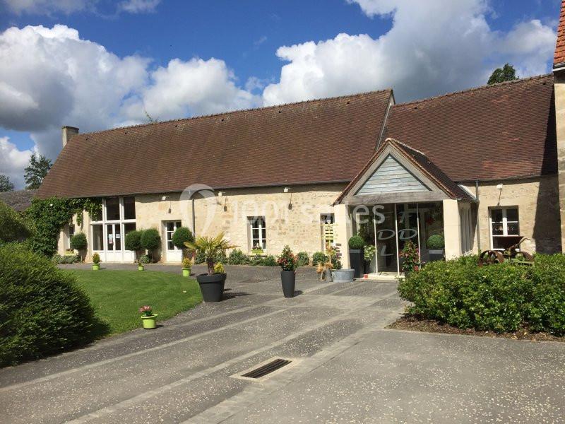 Bâtiment en pierre avec toit en tuiles, entouré de verdure et d'un chemin pavé sous un ciel partiellement nuageux.