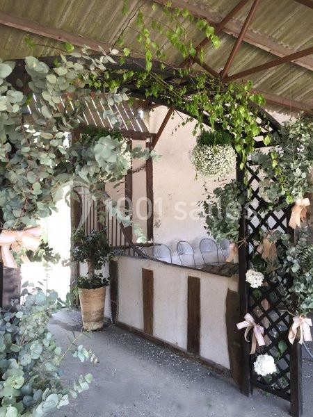 Arche décorée de feuillage et de fleurs blanches sous un abri en tôle, avec des chaises en arrière-plan.