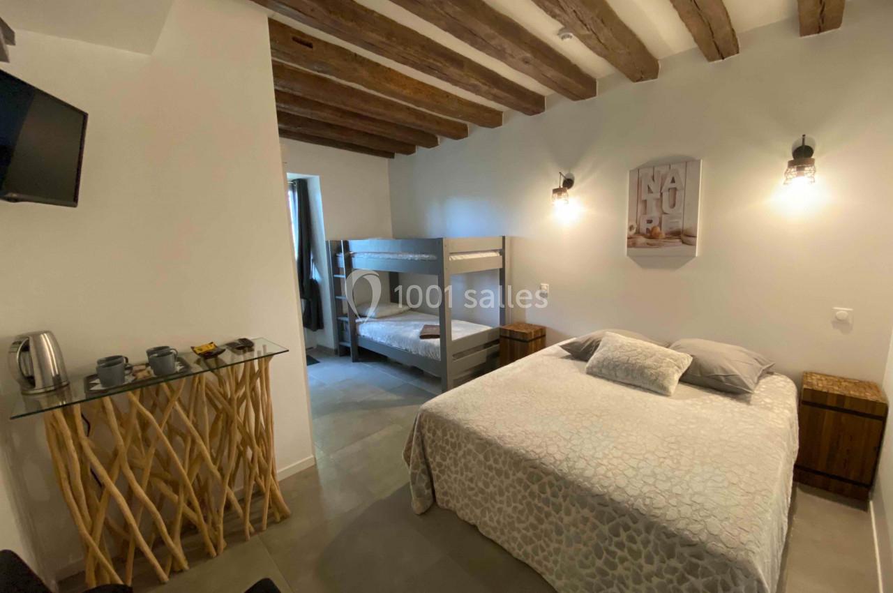 Chambre avec lit double, lits superposés, poutres apparentes, table en bois et éclairage mural.