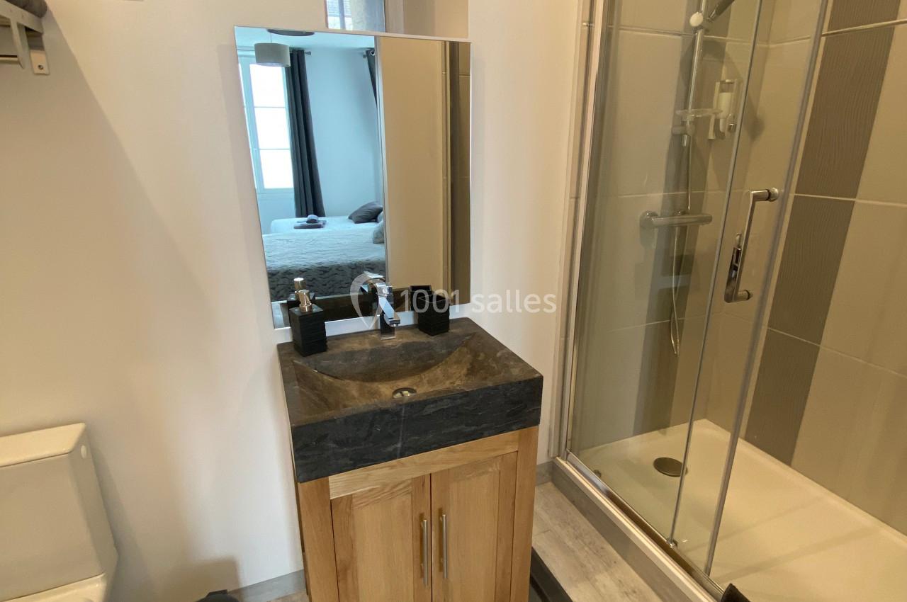 Salle de bain avec douche vitrée, meuble-lavabo en bois, miroir, toilettes et sol en parquet clair.
