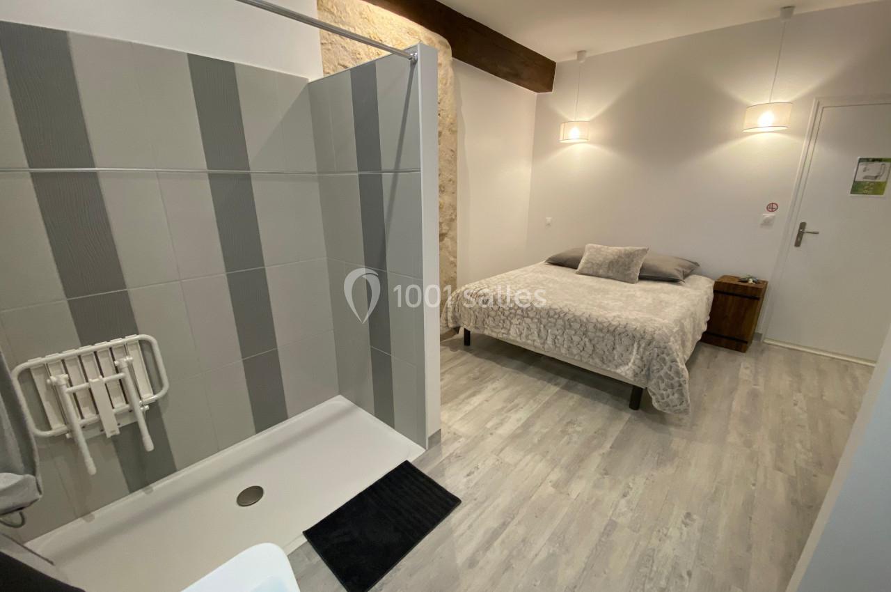 Chambre avec lit double, douche accessible, sol en parquet clair et éclairage moderne.