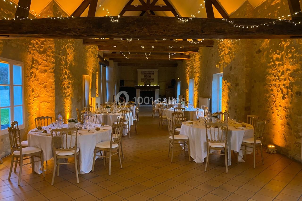 Salle de réception en pierre avec tables dressées, chaises en bois et éclairage chaleureux.