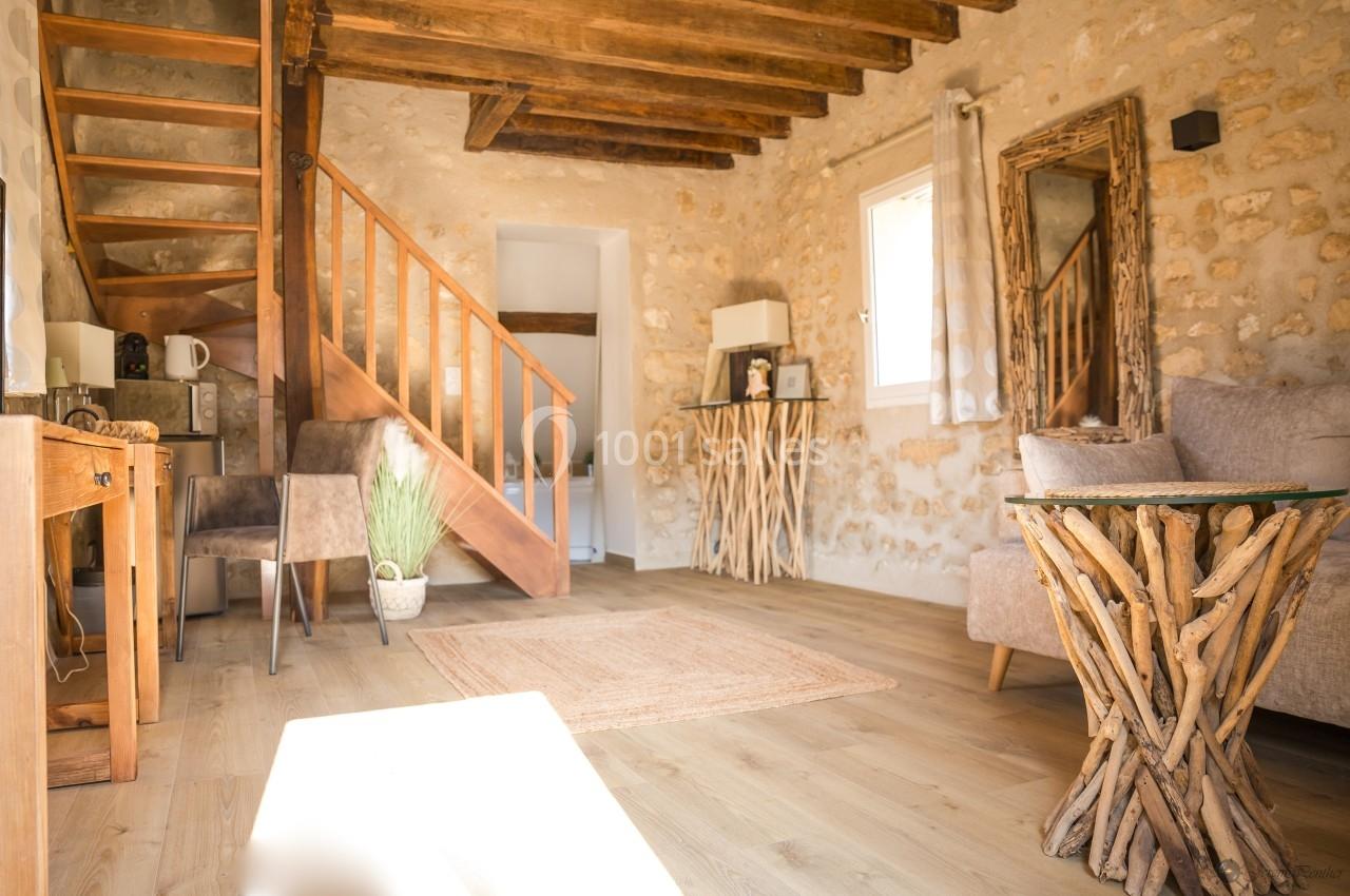 Salon lumineux avec murs en pierre, mobilier en bois et décoration naturelle, comprenant un escalier et une fenêtre.