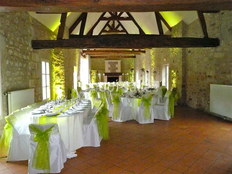 Salle de réception en pierre avec tables dressées et chaises décorées de nœuds verts, éclairage chaleureux.