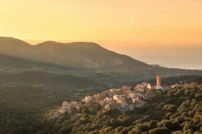 Paysage montagneux au coucher du soleil avec une personne debout sur un promontoire rocheux, entourée de végétation.
