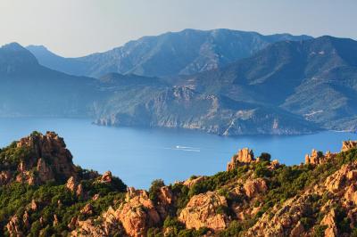 Paysage montagneux au coucher du soleil avec une personne debout sur un promontoire rocheux, entourée de végétation.