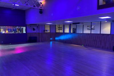 Salle de danse avec parquet clair, miroirs, sièges noirs et un portrait mural de Che Guevara.