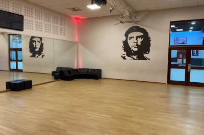 Salle de danse avec parquet clair, miroirs, sièges noirs et un portrait mural de Che Guevara.