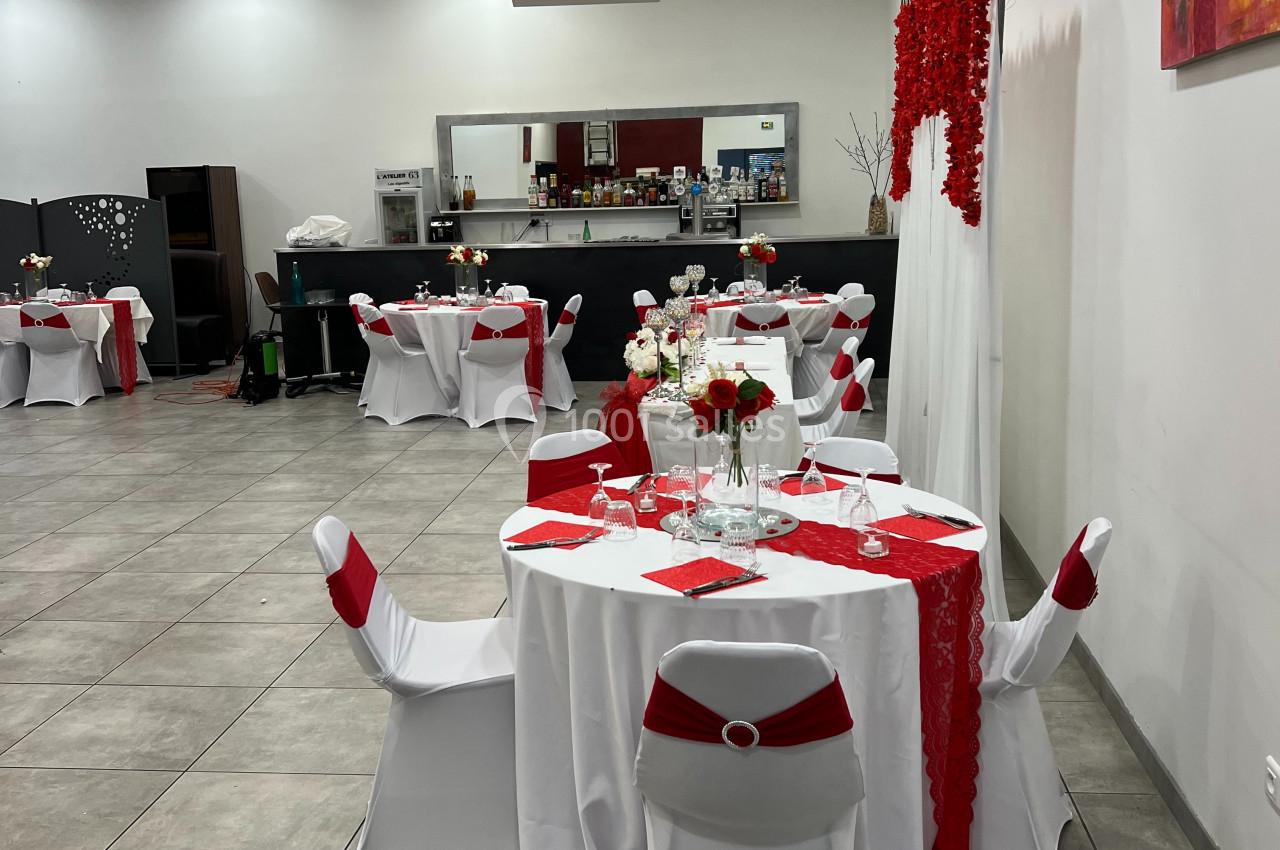 Salle de réception décorée en rouge et blanc avec tables dressées, nappes blanches et chemins de table rouges.