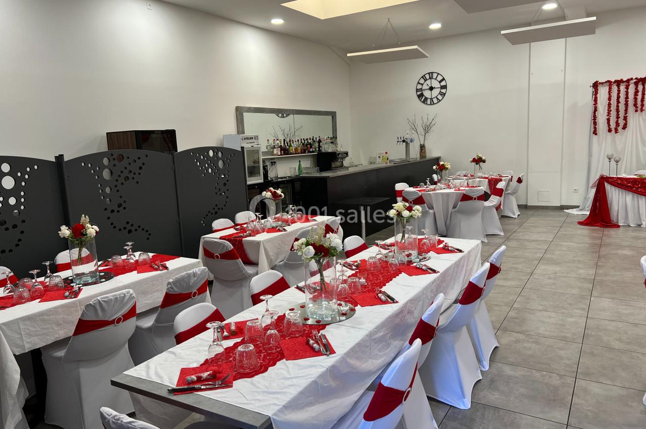 Salle de réception décorée avec des tables dressées en rouge et blanc, prête pour un événement festif.