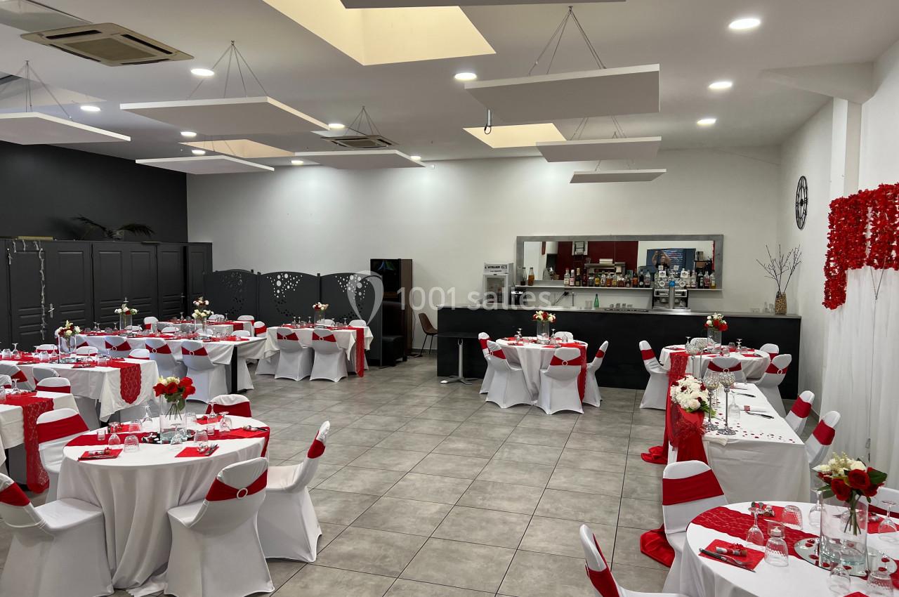 Salle de réception décorée en rouge et blanc, avec tables dressées et un bar en arrière-plan.