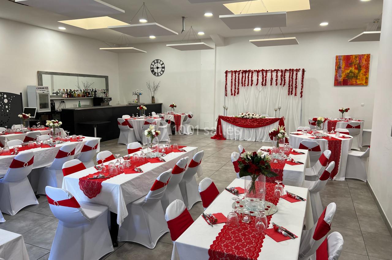 Salle de réception décorée en rouge et blanc avec tables dressées, chaises houssées et un espace pour le buffet.