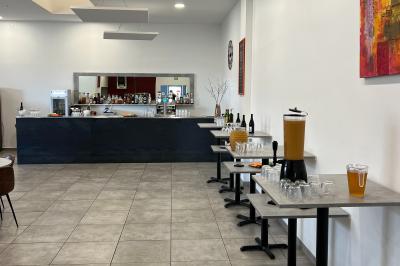 Comptoir de bar avec bouteilles alignées, verres, machine à café et décor sobre dans une pièce lumineuse.