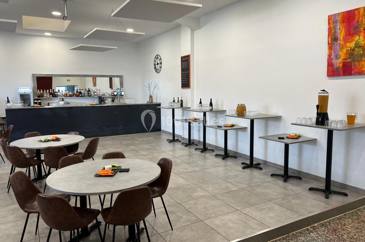 Salle lumineuse avec tables rondes, chaises en cuir marron, buffet avec boissons et décorations murales colorées.