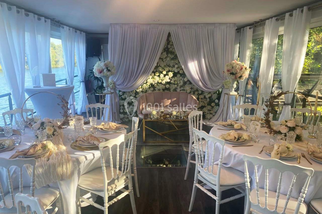 Salle décorée pour un mariage avec des tables élégantes, des chaises blanches, des fleurs et une arche florale blanche.