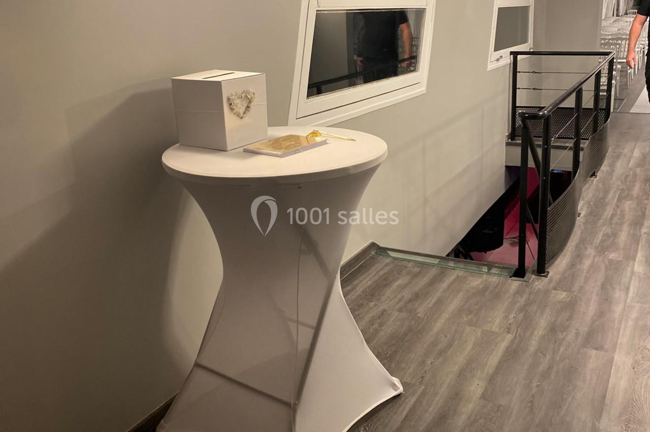 Table haute recouverte d'une housse blanche, avec une boîte décorative et un stylo, dans un couloir moderne.