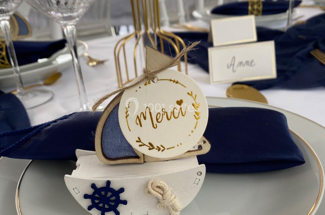 Décoration de table avec un marque-place en forme de bateau en bois, portant l'inscription ’Merci’, sur une assiette.