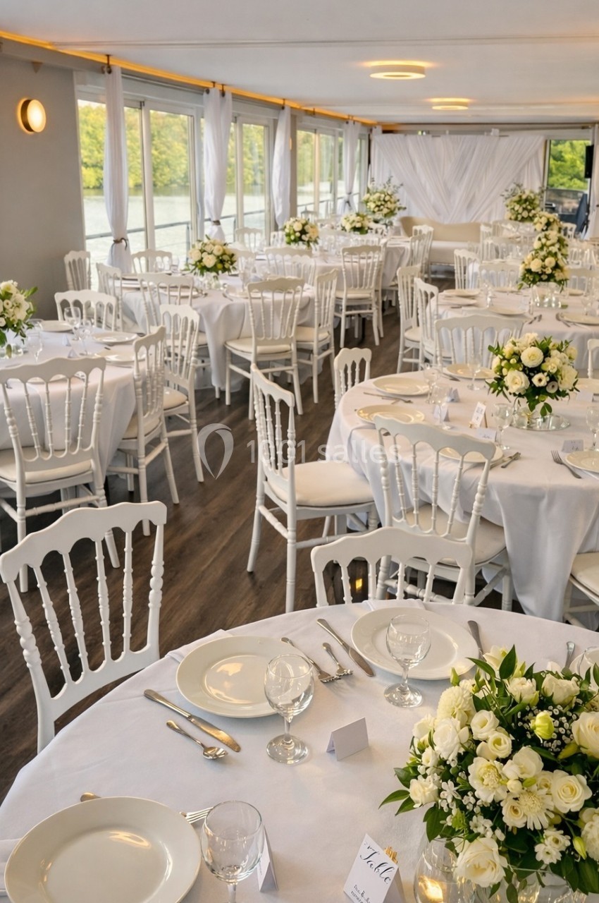 Salle de réception élégante avec des tables rondes dressées, décorées de nappes blanches et de bouquets de fleurs.