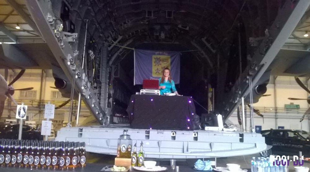 Une DJ anime un événement à l'intérieur d'un avion cargo, avec des bouteilles disposées au premier plan.