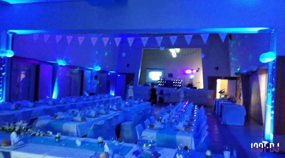 Salle décorée pour un événement avec tables dressées, nappes bleues et éclairage tamisé aux tons bleus.