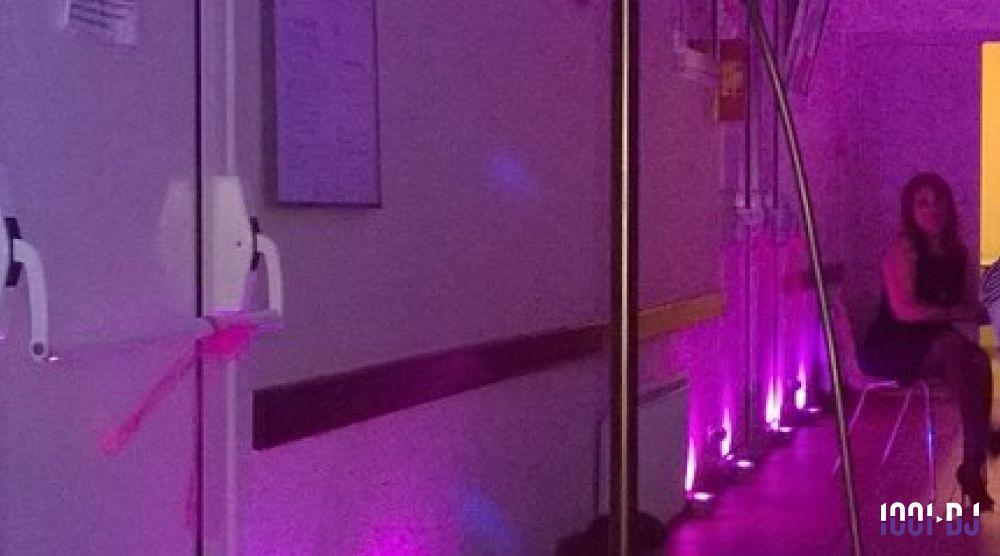 Couloir éclairé par des lumières violettes, avec une femme assise sur une chaise à droite.