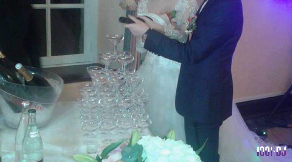 Un couple en tenue de mariage remplit une pyramide de coupes avec du champagne lors d'une réception.