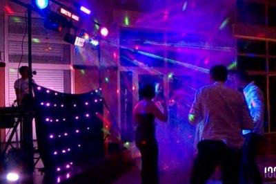 Un couple danse dans une salle faiblement éclairée avec des lumières colorées et une ambiance festive.