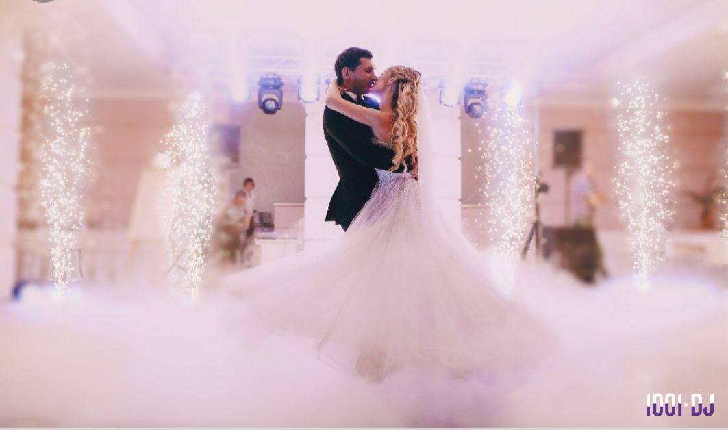 Un couple danse dans une salle éclairée, entouré de fumée au sol et de colonnes lumineuses.