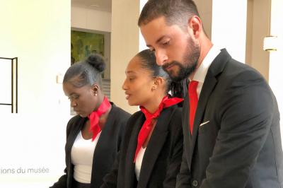 Quatre femmes en robe noire sourient debout sur une terrasse en bois avec un fond de verdure.