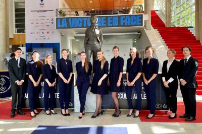 Quatre femmes en robe noire sourient debout sur une terrasse en bois avec un fond de verdure.