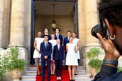 Quatre femmes en robe noire sourient debout sur une terrasse en bois avec un fond de verdure.