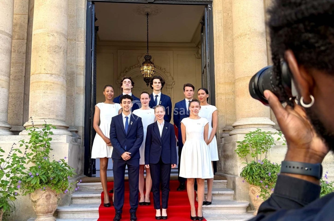 Un groupe de personnes posant sur un tapis rouge devant une entrée monumentale, photographié par un photographe.