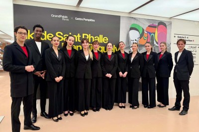 Quatre femmes en robe noire sourient debout sur une terrasse en bois avec un fond de verdure.