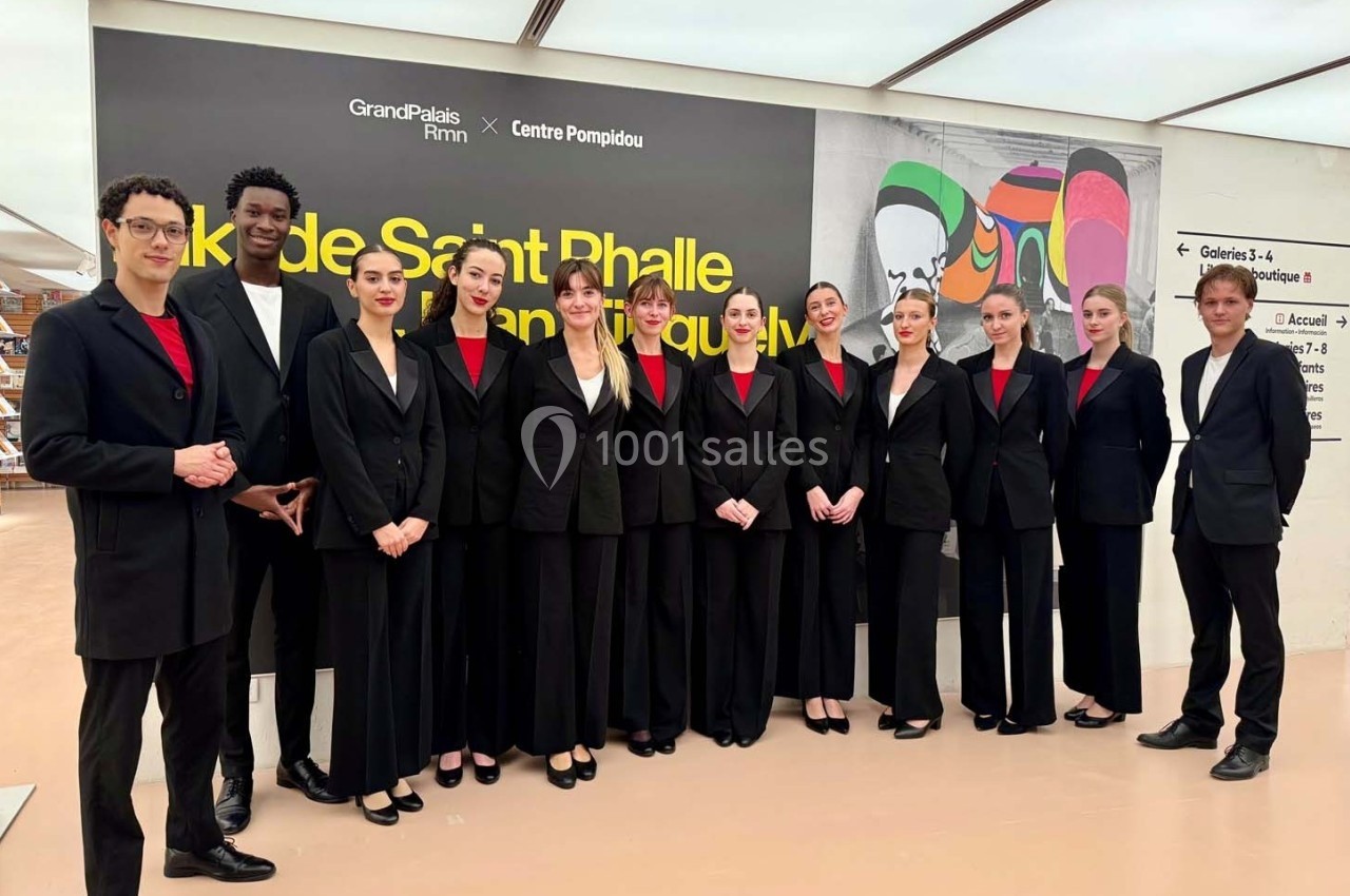 Un groupe de personnes en tenue formelle pose devant un mur affichant une exposition au Grand Palais Immersif.