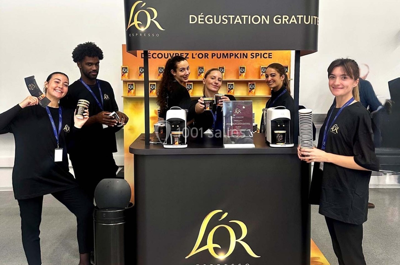 Équipe souriante devant un stand proposant une dégustation gratuite de café avec machines et gobelets exposés.