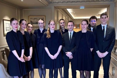 Quatre femmes en robe noire sourient debout sur une terrasse en bois avec un fond de verdure.