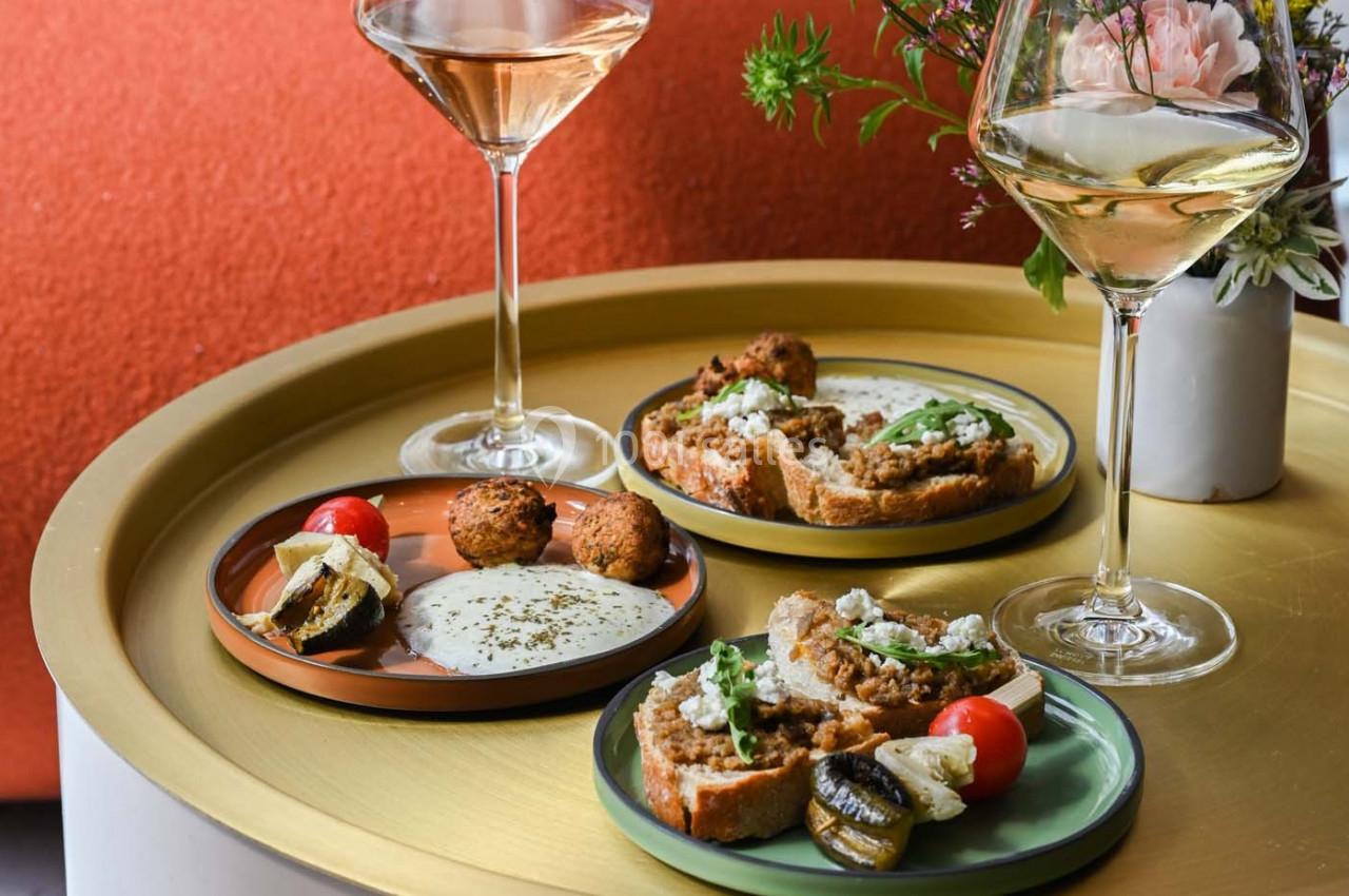Assiettes de mezzés avec tartines, falafels, légumes grillés et sauces, servies avec des verres de vin blanc.